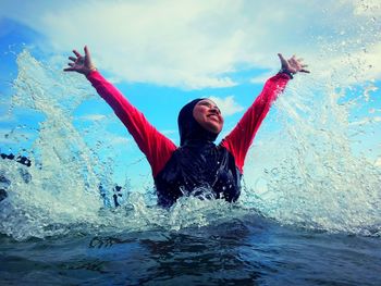 Happy woman with arms raised against sky in sea