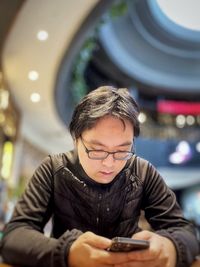 Young asian man using smartphone at table against architectural features.