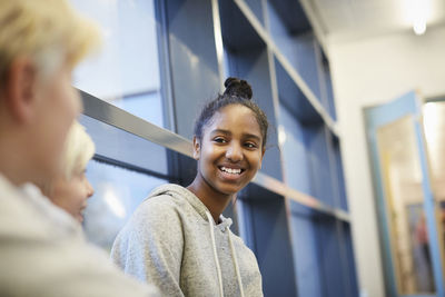 Smiling middle school girl talking with male friends in corridor