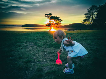 Rear view of girl on shore against sky during sunset