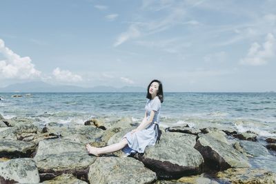 Beautiful woman sitting on rocks at beach