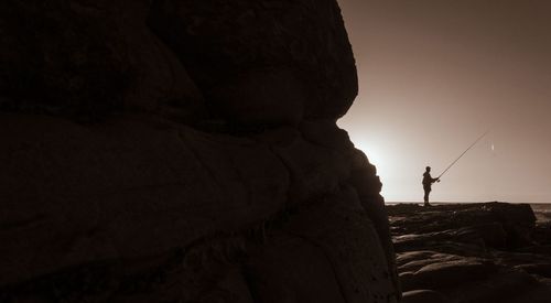 Rear view of silhouette man on rock formation against sky