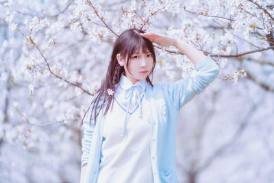 Portrait of young woman standing by cherry blossom tree