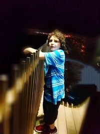 Portrait of teenage girl standing against railing at night