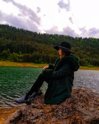 Woman wearing hat while standing by lake against sky