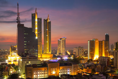Illuminated modern buildings in city against sky during sunset