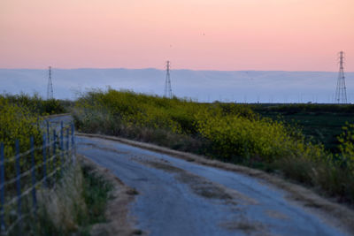 Road amidst field against sky during sunset