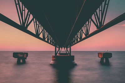 Bridge over sea against sky during sunset