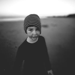 Portrait of boy wearing knit hat standing at beach against sky