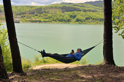 Young man using mobile phone while relaxing in hammock near lake