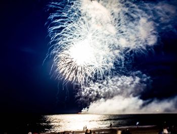 Low angle view of fireworks in sea against sky at night