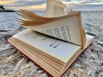 Close-up of open book on rock at beach during sunset