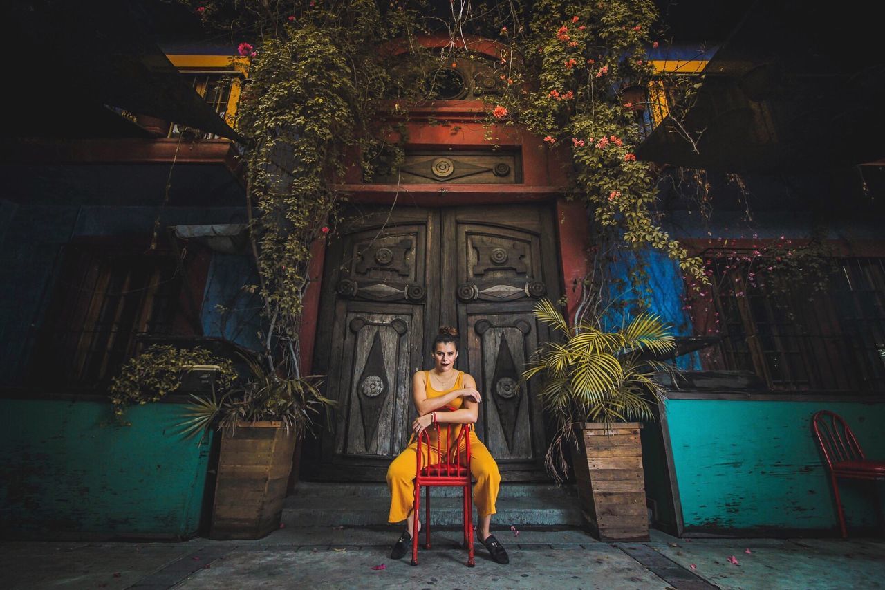 PORTRAIT OF WOMAN SITTING BY BUILDING