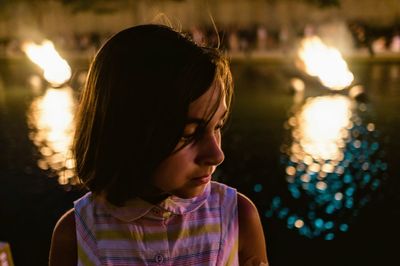 Close-up of girl looking away at night by swimming pool