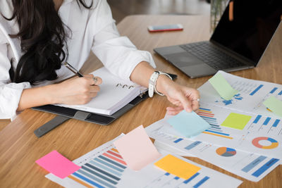 Midsection of businesswoman writing on diary while sitting at desk in office