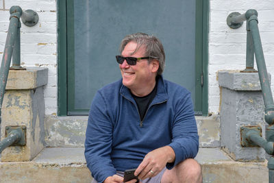 Smiling man in sunglasses sitting against house