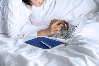 Midsection of woman using laptop on bed