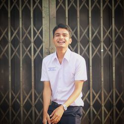 Portrait of smiling man standing against fence