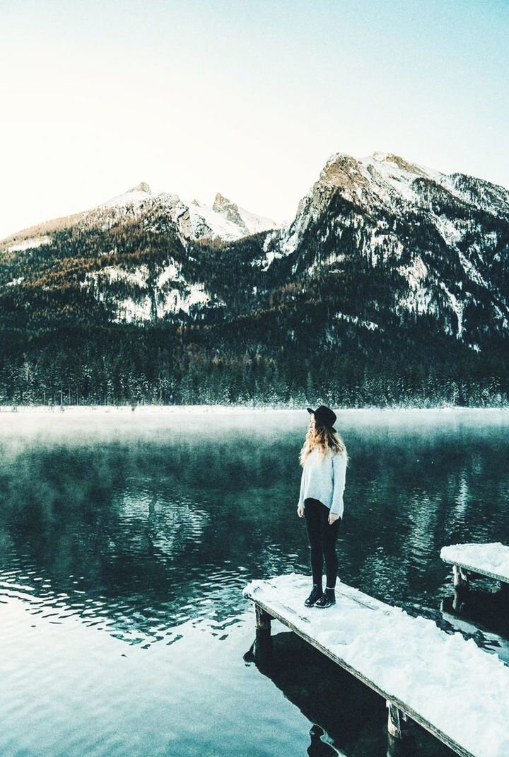 water, mountain, one person, lake, snow, beauty in nature, scenics - nature, full length, nature, sky, winter, cold temperature, adult, leisure activity, standing, reflection, rear view, tranquility, day, mountain range, tranquil scene, lifestyles, vacation, trip, women, men, non-urban scene, environment, travel, holiday, landscape, outdoors, young adult, idyllic, travel destinations, solitude, casual clothing, remote, relaxation, looking at view, clear sky