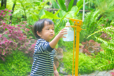 Side view of cute boy holding plant in yard