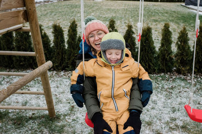 Mother and son playing outside laughing whilst on a swing set