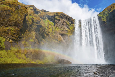 Low angle view of beautiful skogafoss waterfall falling from cliffs against sky