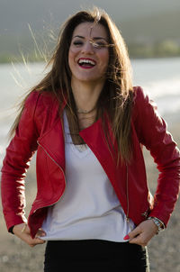 Cheerful woman in red leather jacket laughing while standing at beach