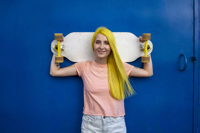 Portrait of young woman standing against blue wall