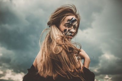 Portrait of woman with messy face against cloudy sky