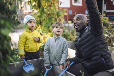 Male teacher talking with preschool kids holding shovel at garden