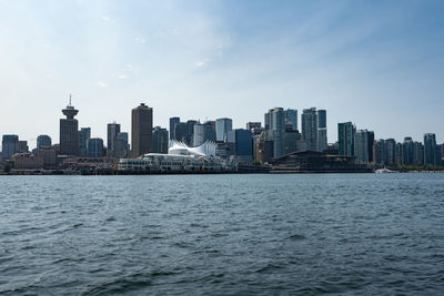 Sea by modern buildings in city against sky