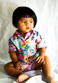 Portrait of cute baby girl sitting on bed at home