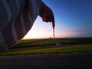 Silhouette person holding umbrella on land against sky during sunset