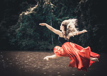 Young ballet dancer wearing red skirt while dancing in forest