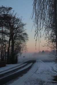 Snow covered road against sky during sunset