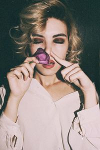 Close-up of young woman smelling purple flower against wall