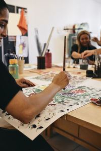 Female painter painting on paper at table in art class