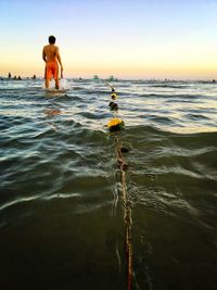 Boy standing on beach against clear sky during sunset