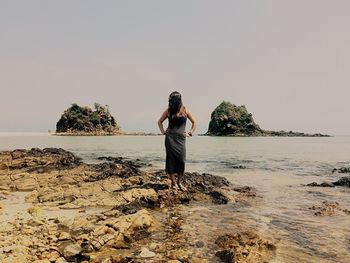 Rear view of woman standing on beach against clear sky