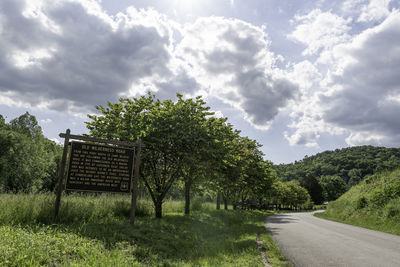 Road amidst trees on field against sky