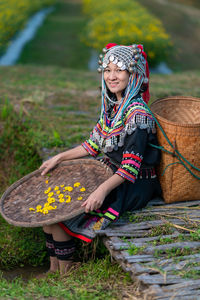 Portrait of smiling woman in traditional clothing holding wicker basket while sitting in farm