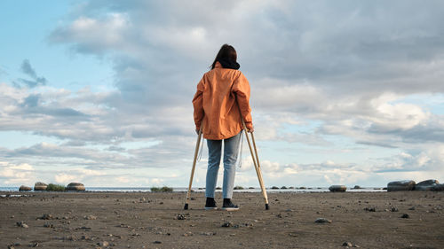 A woman on crutches walks along the shore of the lake. 