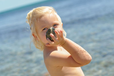 Portrait of shirtless girl holding pebble at beach