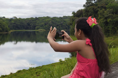 Latin girl with pink dress and cell phone in hand taking photo of a lake in the middle of nature	
