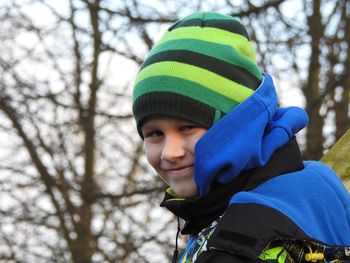 Side view portrait of boy wearing warm clothing against bare trees