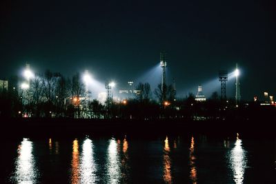 Illuminated factory by city against sky at night