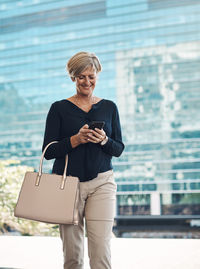 Smiling businesswoman using smart phone while walking on road