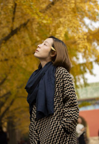 Side view of young woman looking away while standing on tree during autumn