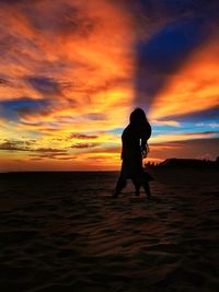 Silhouette woman standing on beach against cloudy sky during sunset