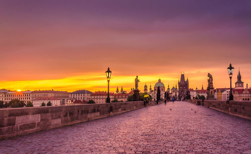 Charles bridge by historic buildings in city against orange sky during sunset